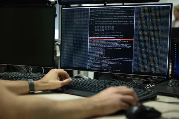 A person typing on a keyboard in front of monitors displaying lines of code