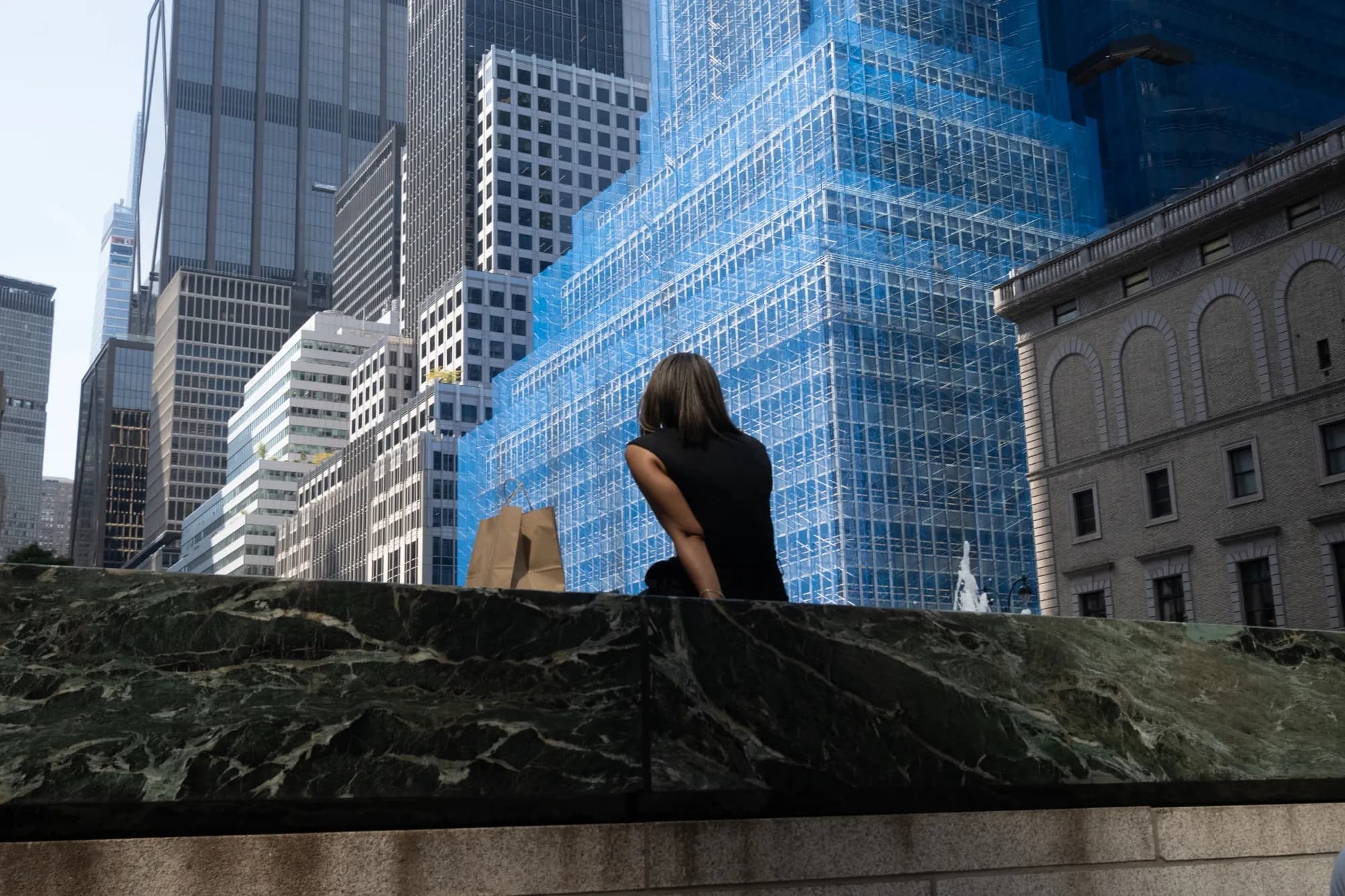 A woman sitting on a ledge in New York's Financial District with skyscrapers behind her